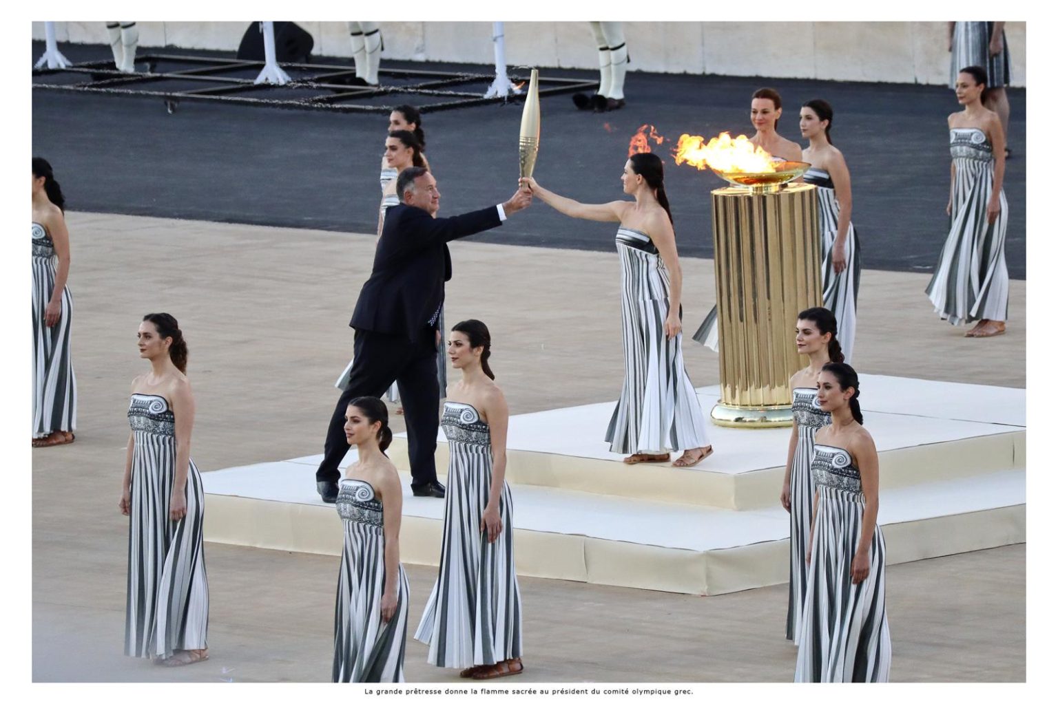 La grande prêtresse donne la flamme sacrée au président du comité olympique grec.